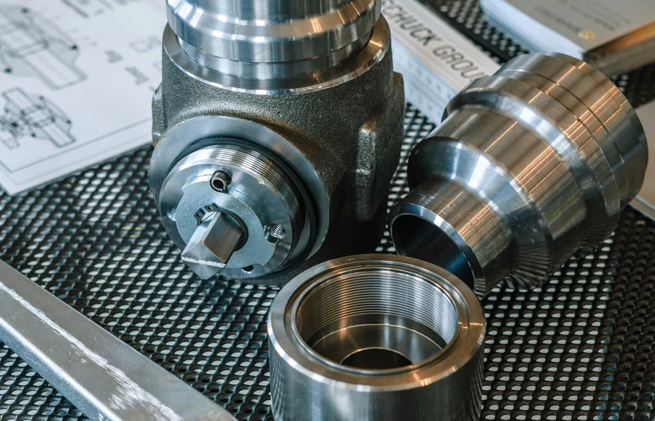 Machined metal components laid out on a workbench beside a dimensioned engineering drawing
