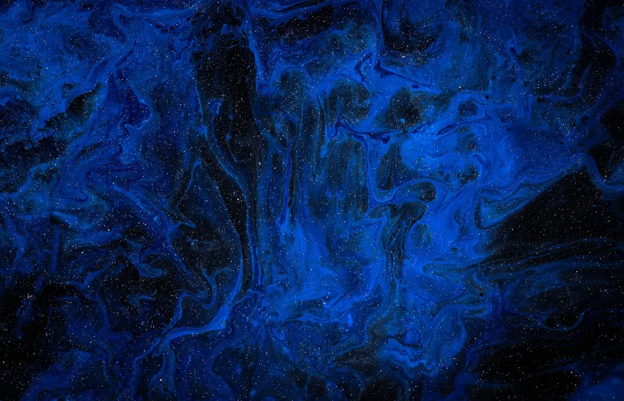 Close up of deep blue marbled paint flecked with fine white speckles against a near black background