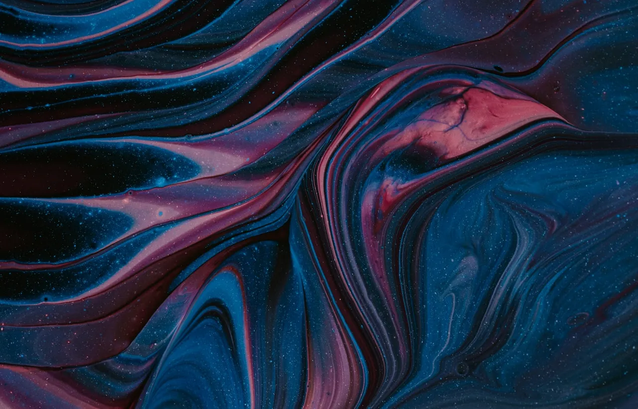 Macro photograph of swirled blue and magenta paint forming layered ridges on a dark surface