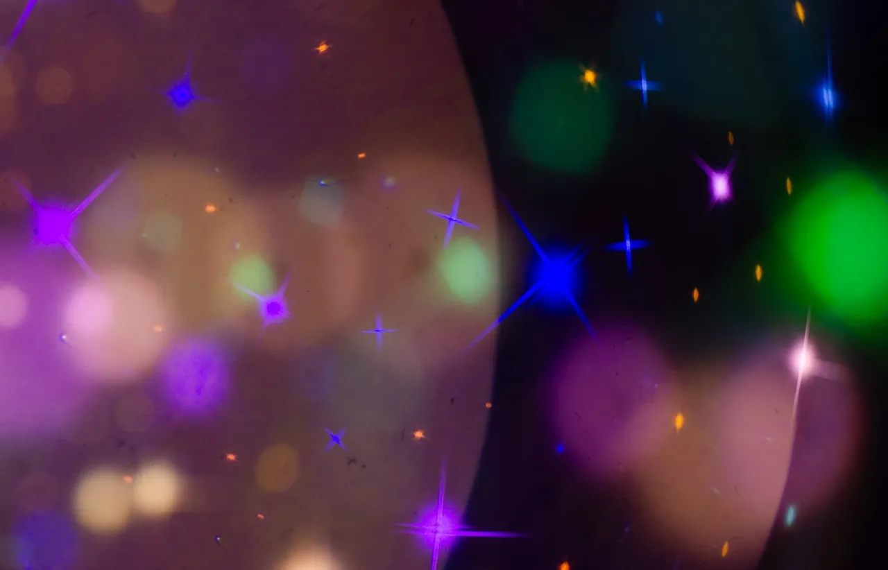Abstract starburst and bokeh lights in violet, blue, and green scattered across a dark frame