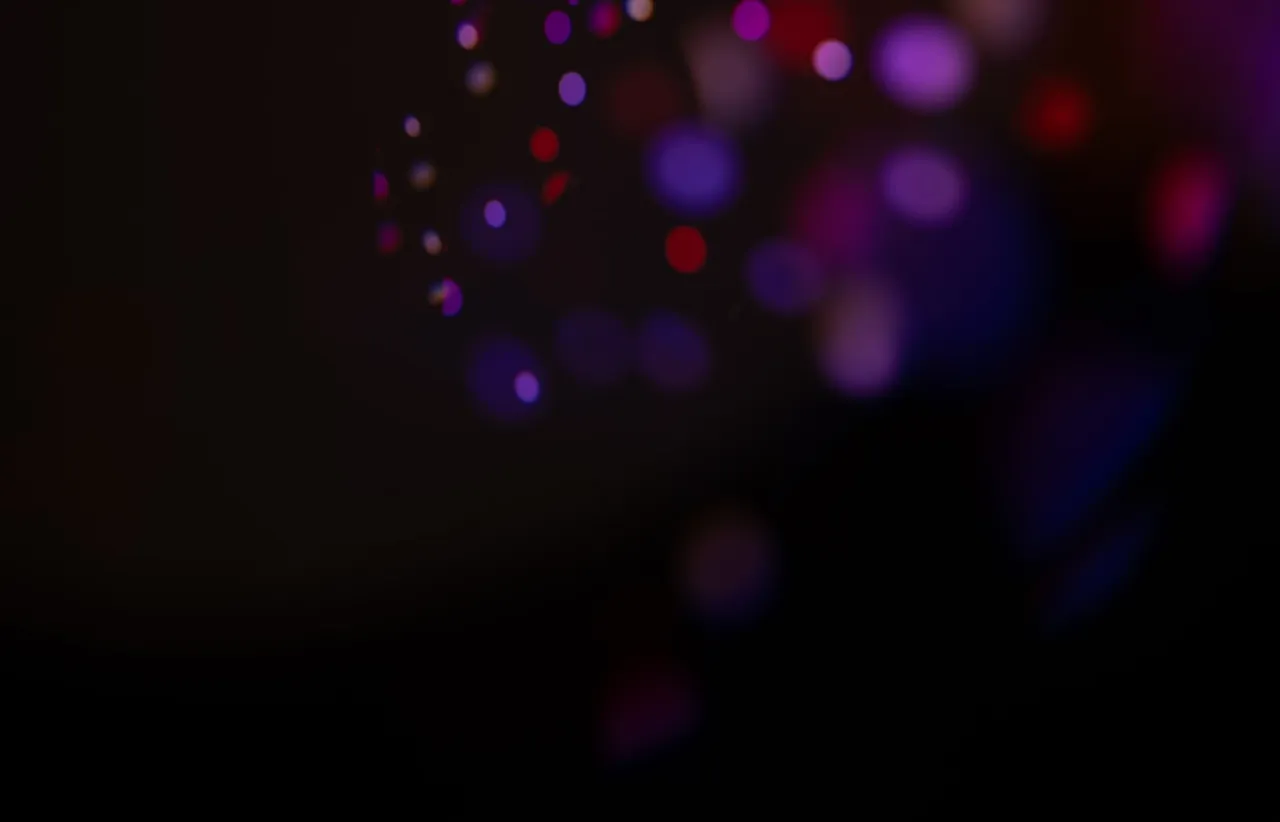 Dispersed violet and blue points of light fading into deep shadow