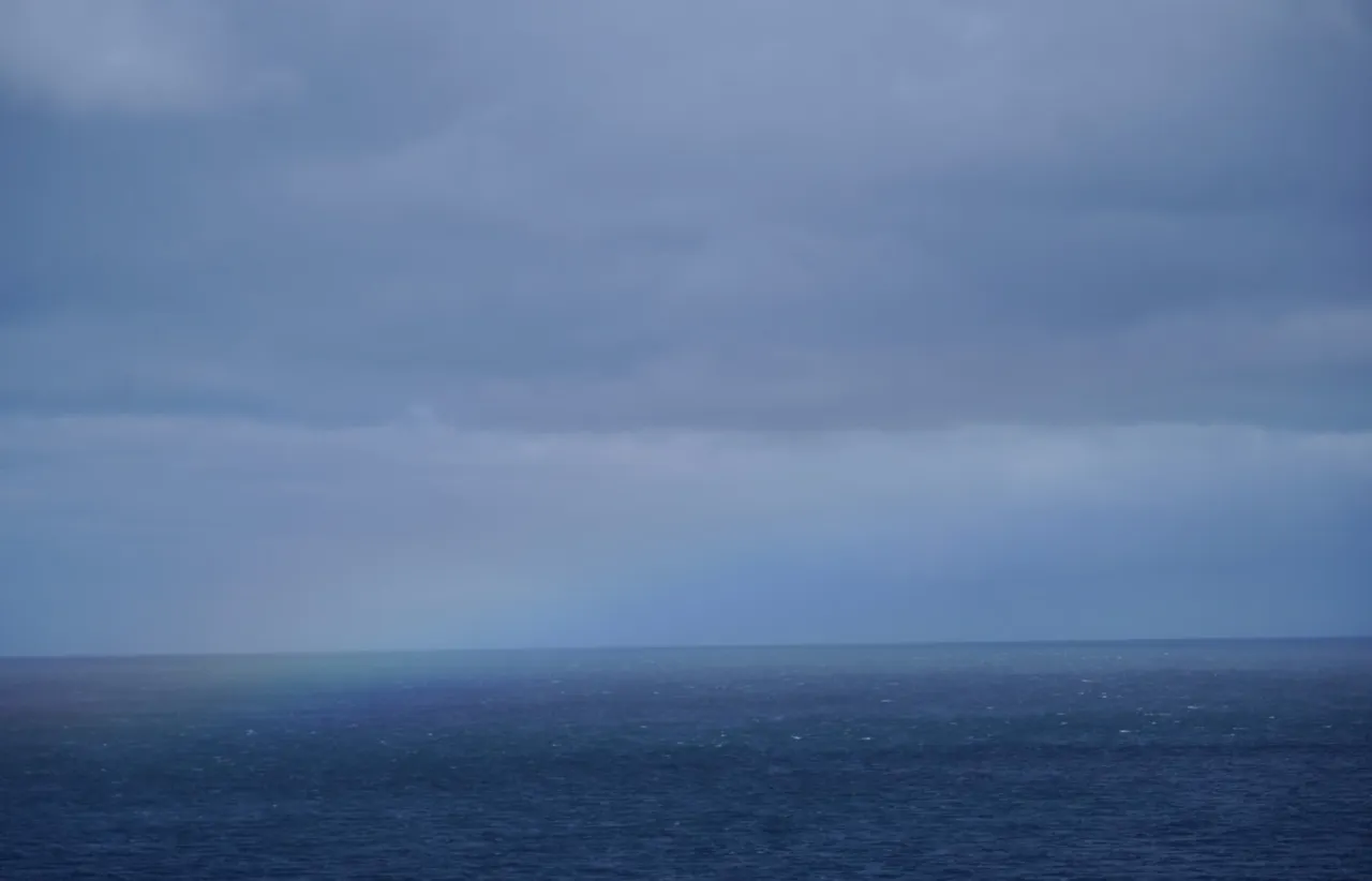 Heavy dark storm clouds hanging low over a flat calm ocean, split by a soft grey horizon line