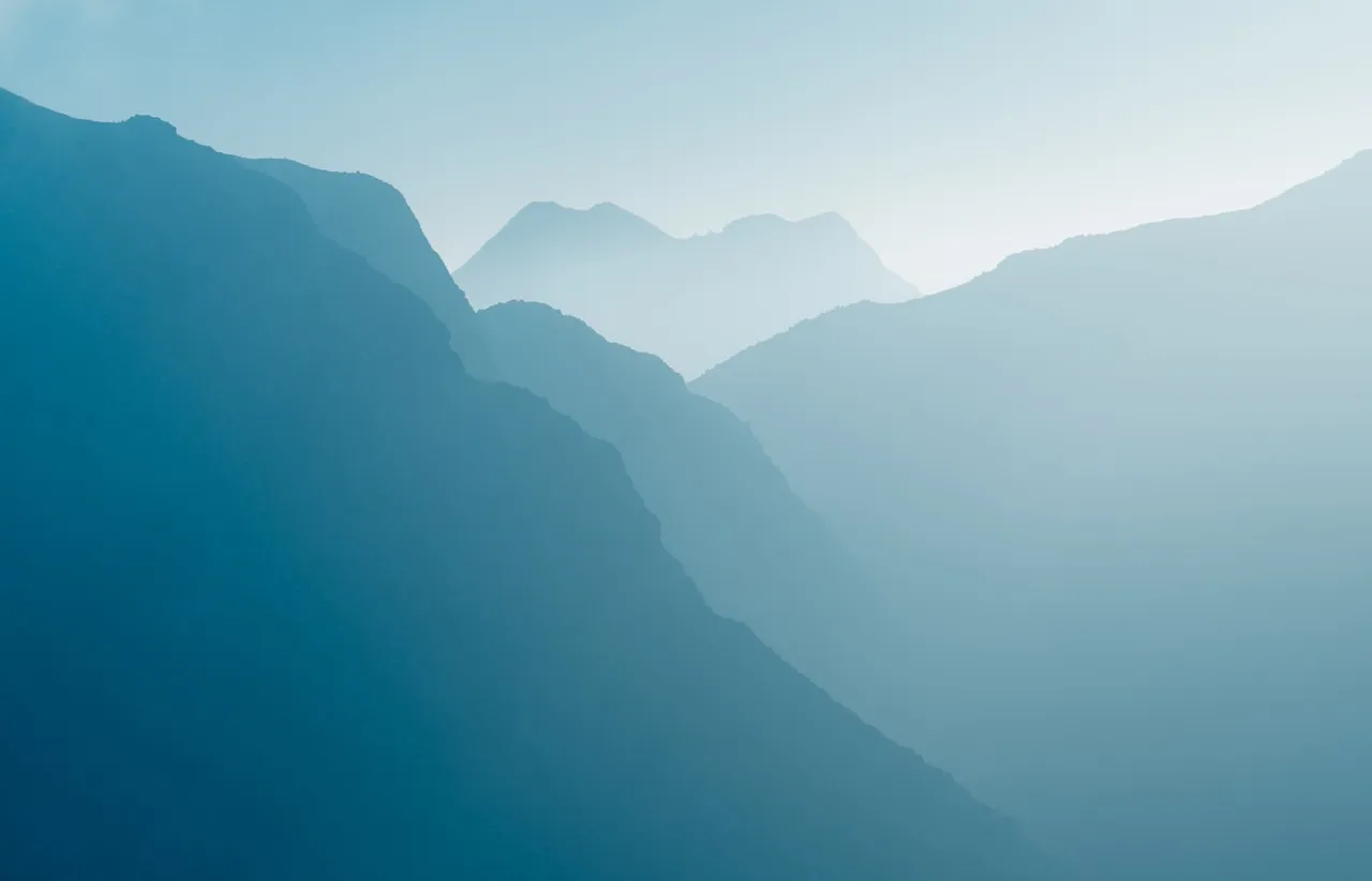Receding layers of grey mountain ridges fading progressively into pale fog on an overcast morning