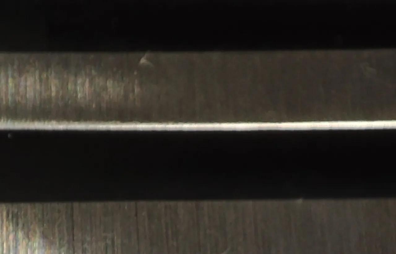 Extreme close up of stacked brushed steel bars with a fine directional grain and deep black shadow gaps between them